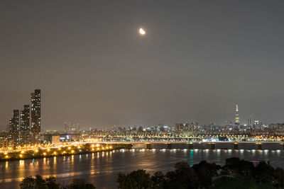 Illuminated buildings by river against sky at night