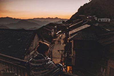 High angle view of woman standing by railing while looking at village during sunset