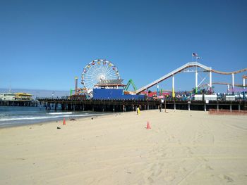 Ferris wheel at beach against clear blue sky during sunny day