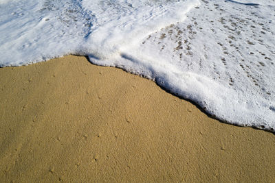 Sea foam waves washing up on sandy beach shore