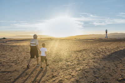 Rear view of man with son waking on beach against lighthouse
