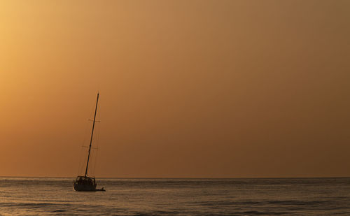 Sailboat in sea against sky during sunrise