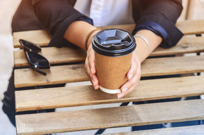 Woman hands holding cardboard cup of coffee in a street cafe. ecological tableware, hot coffee.