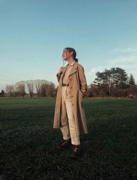 Full length of woman standing on grassy field against sky during sunset