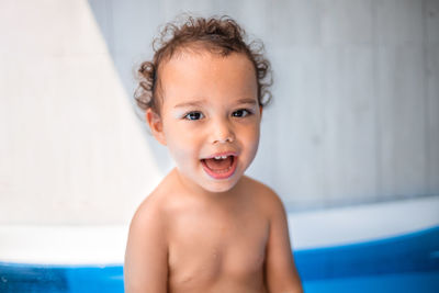 Happy kid playing in an inflatable pool in backyard. curly toddler smiling and playing with water