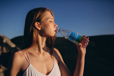 Midsection of woman drinking water from bottle against sky