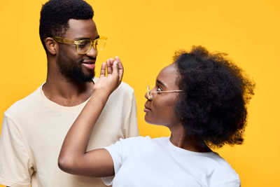 Side view of young man drinking water against yellow background