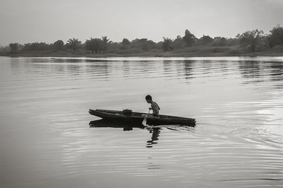 Side view of shirtless man rowing rowboat in lake