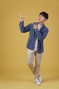 Young man looking away while standing against yellow background