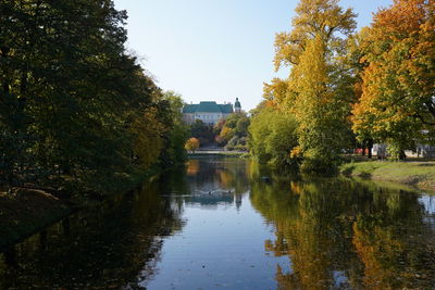 Trees by canal against sky during autumn