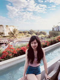 Portrait of young woman standing against river against sky