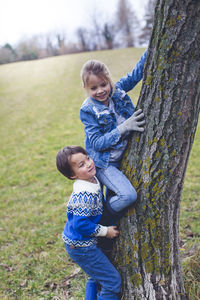 Girl with brother climbing tree on field