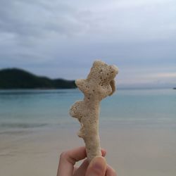 Close-up of hand holding sand at beach against sky