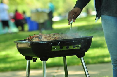 Cropped image of person preparing food on barbeque at park