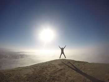 Silhouette woman with arms outstretched standing on landscape at sunset