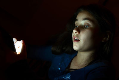 Close-up of teenage girl using illuminated phone against black background