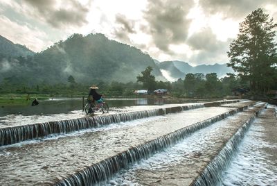 Man on riverbank against sky