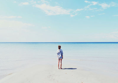 Rear view of girl standing at beach against sky