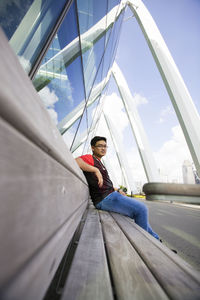 Portrait of young woman sitting on car against sky
