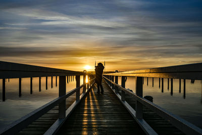 Silhouette man on pier against sky during sunset