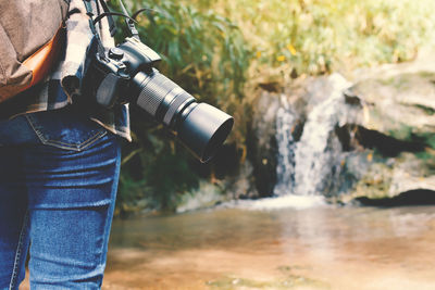 Cropped image man with camera standing by stream