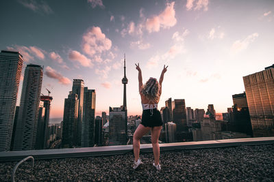 Rear view of man standing by cityscape against sky during sunset