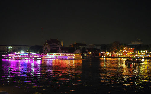 Illuminated city by river against sky at night