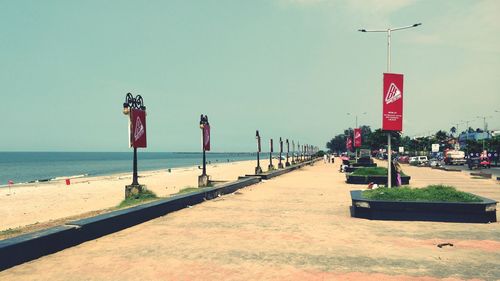 Road sign on street by sea against clear sky