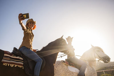 Woman taking selfie while doing horseback riding with friend