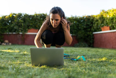 Serious athletic female choosing online tutorial on laptop while preparing for workout in backyard in summer