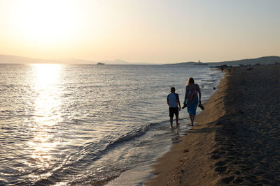 Rear view of women on beach against sky during sunset