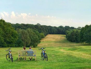 People on bicycle on field against sky