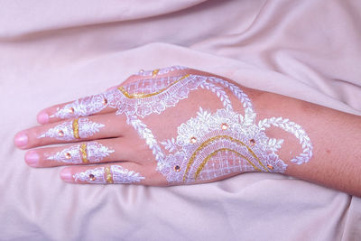 Cropped hand of woman with tattoo over bed