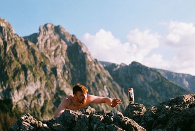 Man standing on rock by mountains against sky