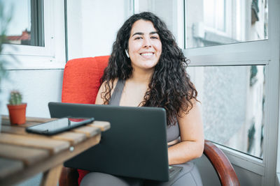 Smiling young woman using laptop sitting on sofa