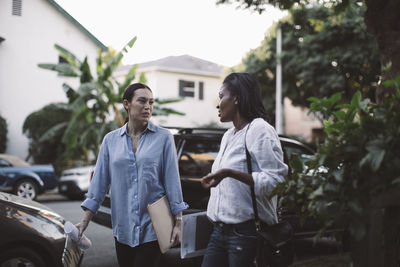 Female designers communicating while walking on footpath against car