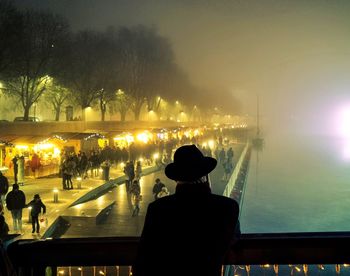 People enjoying at illuminated christmas market during foggy weather