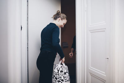 Happy woman carrying shopping bag by door