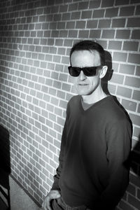 Portrait of young man wearing sunglasses while standing against wall