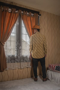 Rear view of woman standing on bed at home