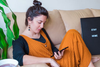 Woman with phone sitting on sofa at home