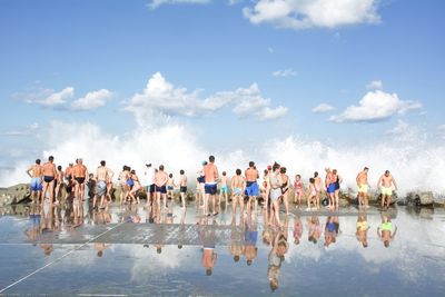 People enjoying at beach against cloudy sky