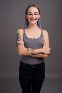 Portrait of smiling young woman standing against gray background