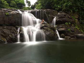 Woman sitting by waterfall on rocks