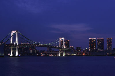 Illuminated tokyo rainbow bridge over rivers and buildings against the backdrop of the night sky