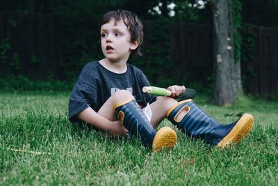 Full length of boy looking away while sitting on grassy field