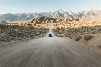 Car on dirt road leading towards mountains