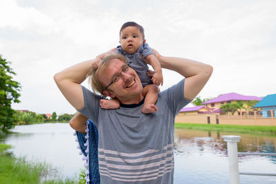 Portrait of father with baby in water against sky