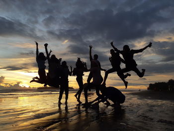 Silhouette people at beach against sky during sunset