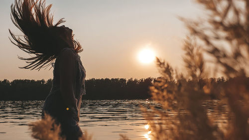 Woman by lake against sky during sunset